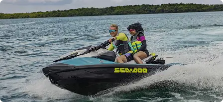 Black two-person jet ski ridden by two people speeding across the open blue sea