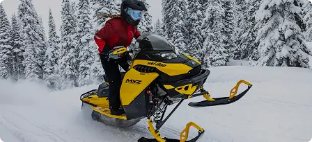 Yellow motorcycle ridden by a person wearing a red coat traveling through a snowy landscape with snow-covered trees