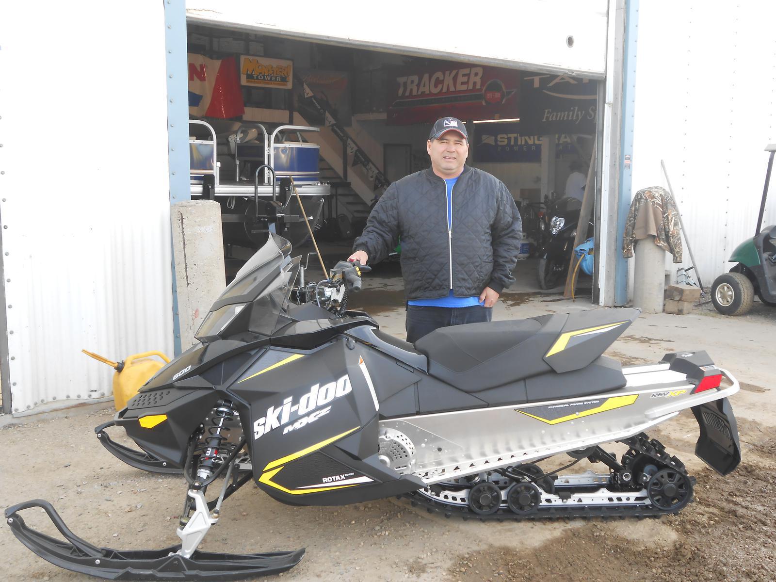 Man standing behind a black Ski-Doo MXZ with yellow accents.