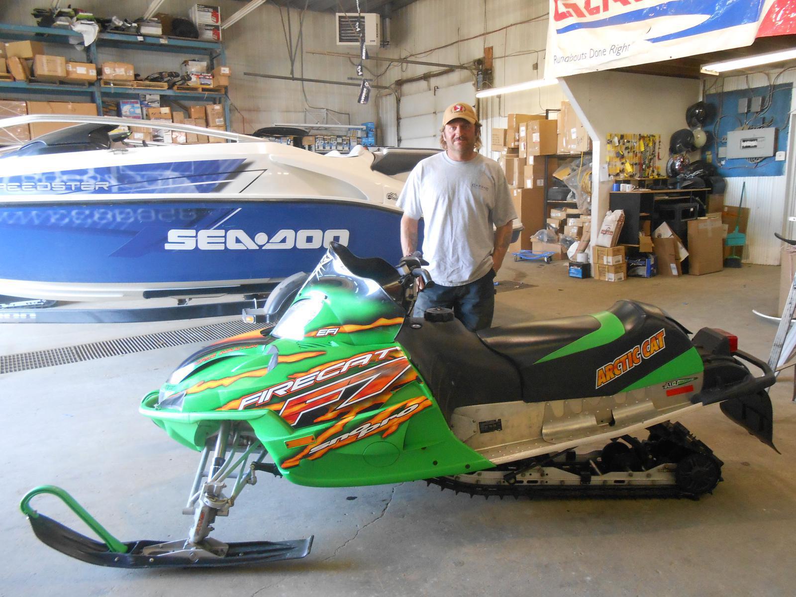 Man standing behind a green Arctic Firecat F7 snowmobile.