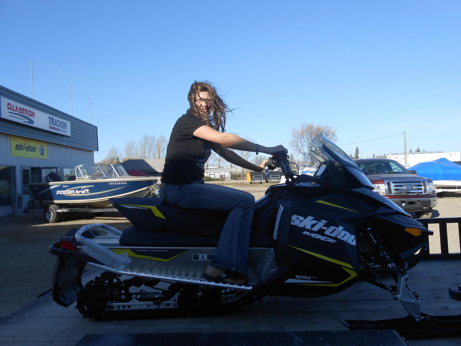 Woman riding a black Ski-Doo MXZ snowmobile with yellow accents.