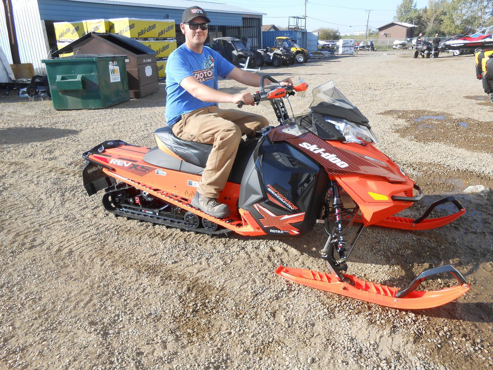 Man riding an orange Ski-Doo Renegade outside a dealership.