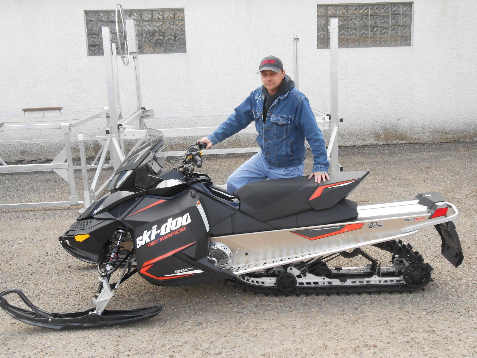 Man posing behind a black Ski-Doo Renegade snowmobile with orange accents.