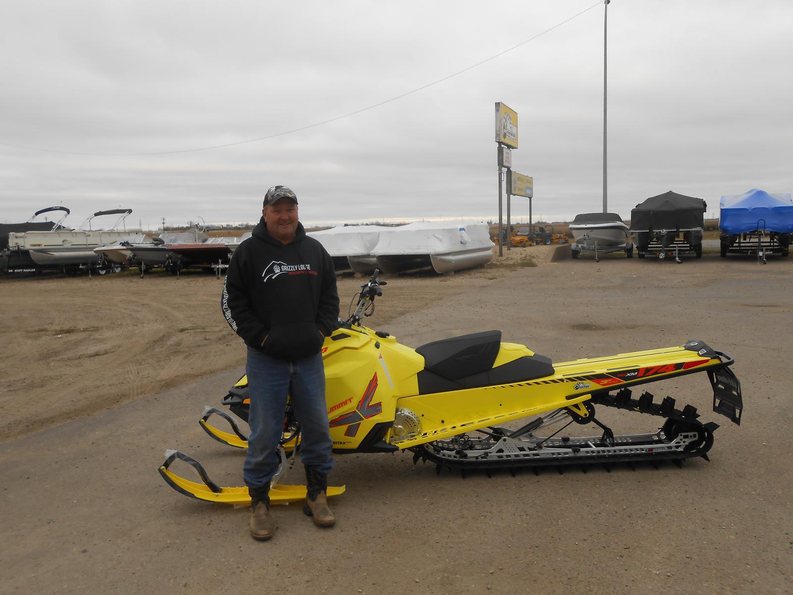 Man standing in front of a yellow Ski-Doo Summit snowmobile.