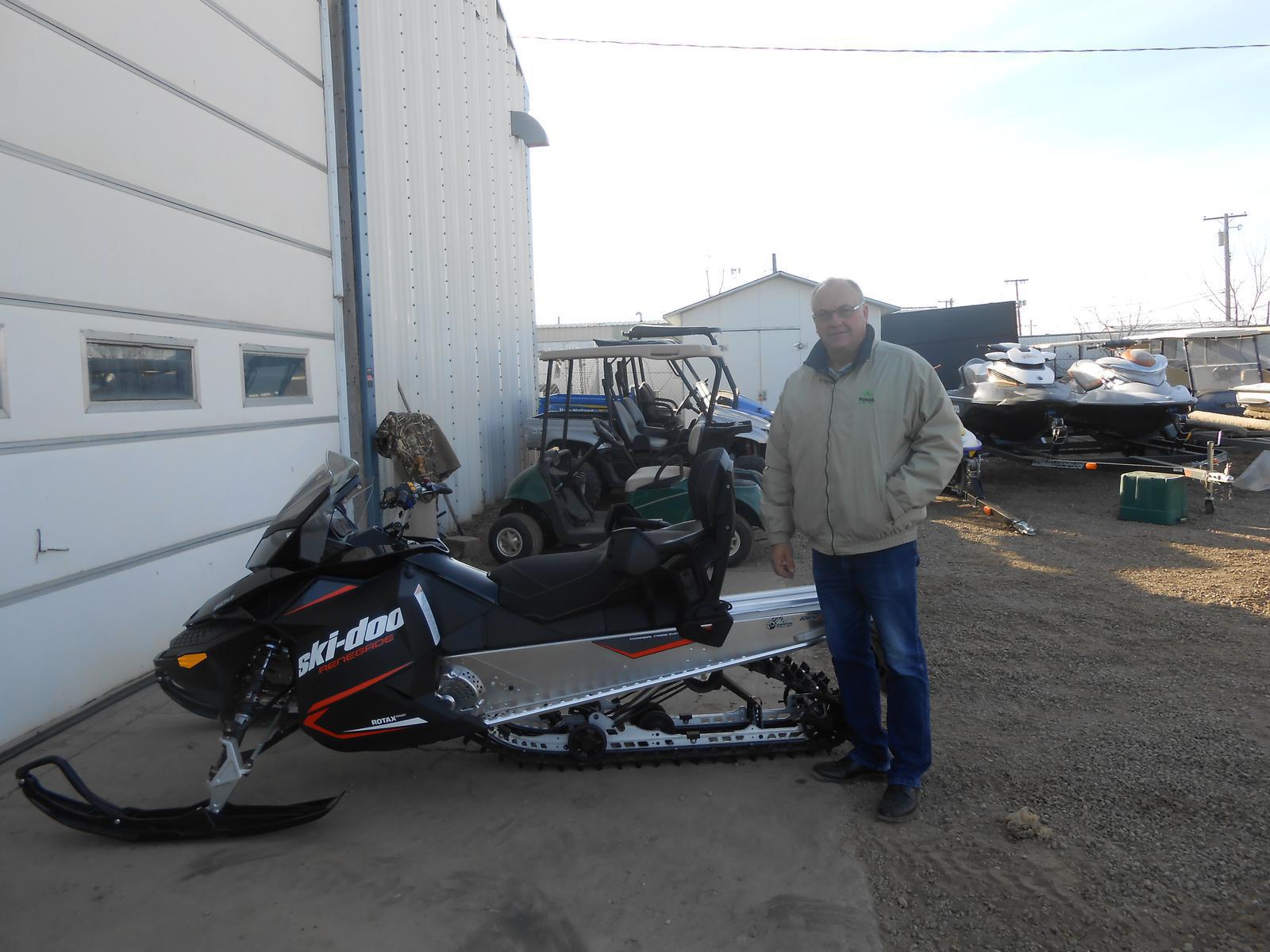 Man standing beside a black Ski-Doo Renegade snowmobile with red accents.