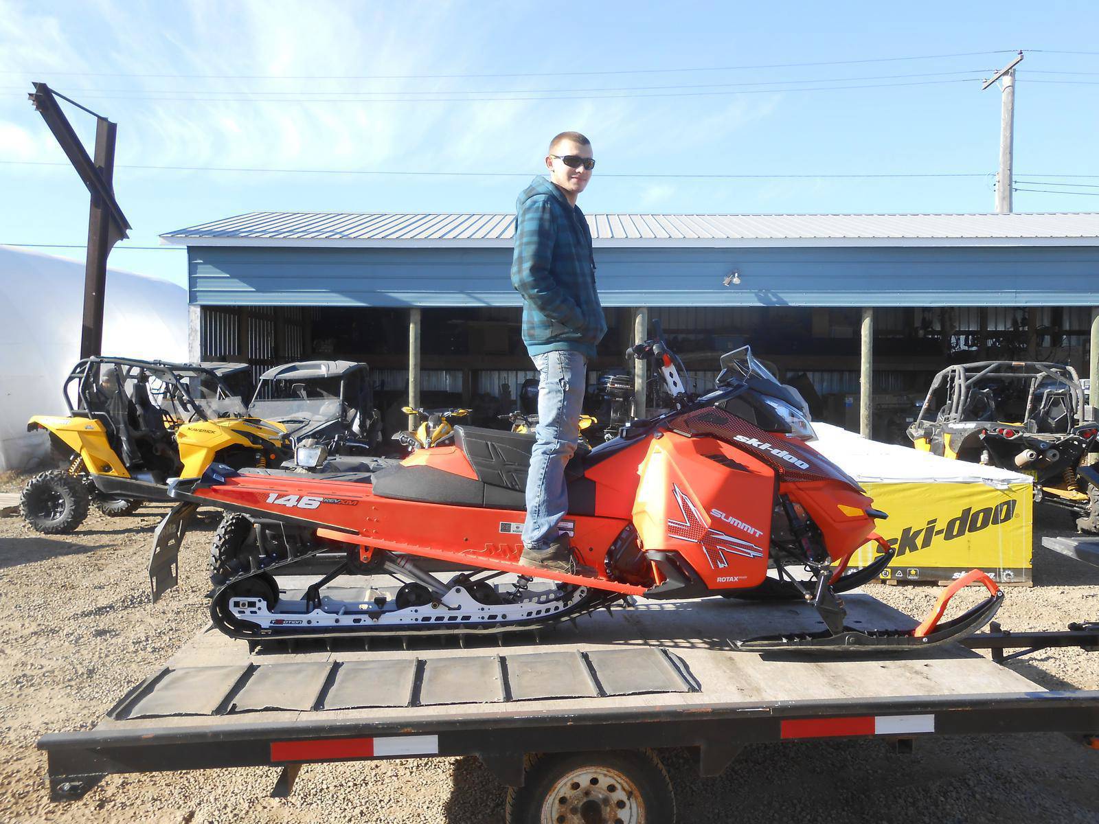 Man standing on an orange Ski-Doo Summit snowmobile outside a dealership.