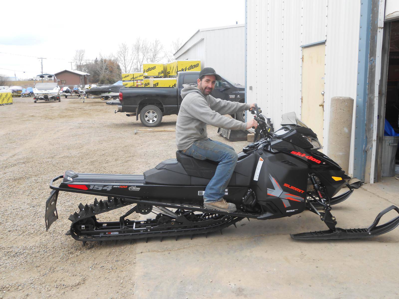 Man sitting on a black Ski-Doo Summit snowmobile outside a dealership.