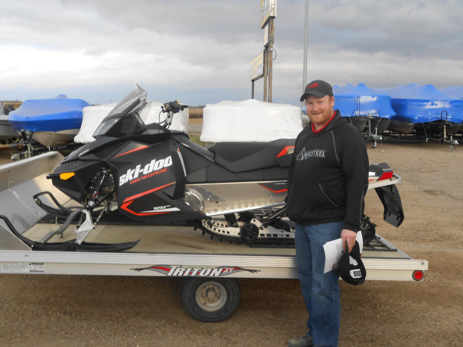 Man standing in front of a black Ski-Doo Renegade snowmobile with red accents.