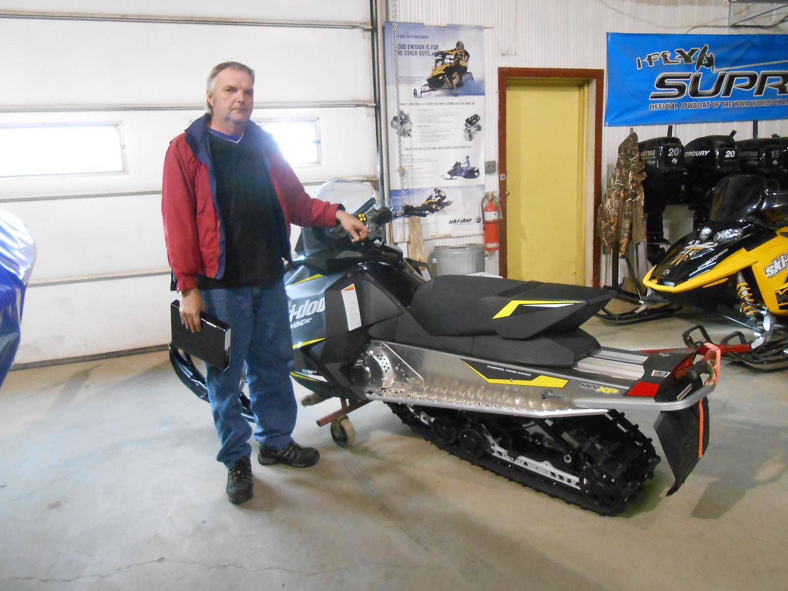 Man standing beside a black and yellow Ski-Doo snowmobile inside a dealership.