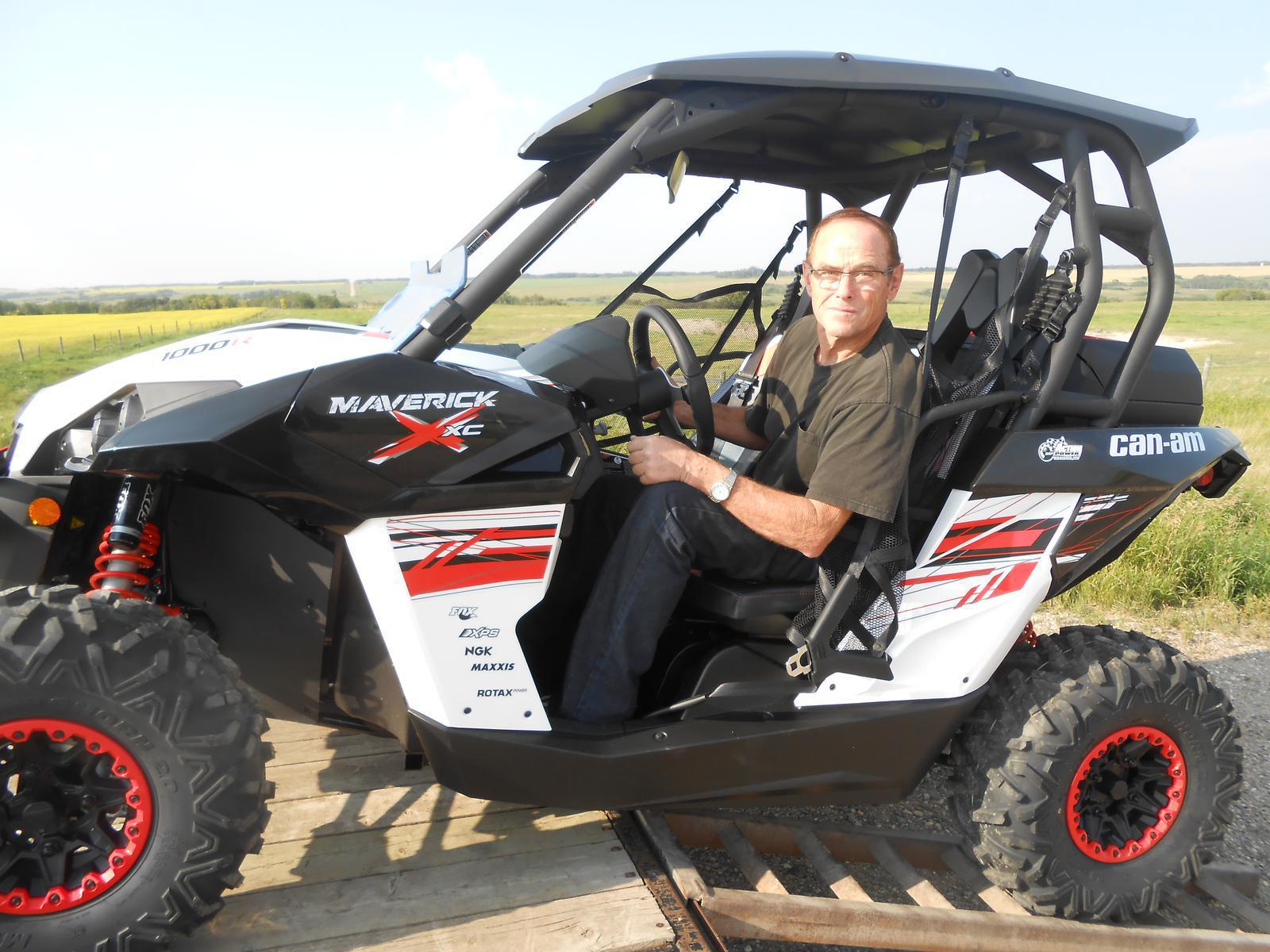 A man seated in a white Can-Am Maverick XC side by side vehicle with red accents.