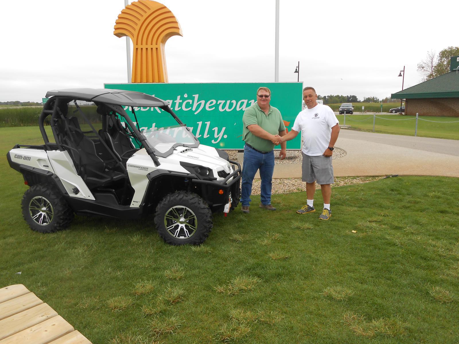 Two men shaking hands beside a white Can-Am Commander UTV