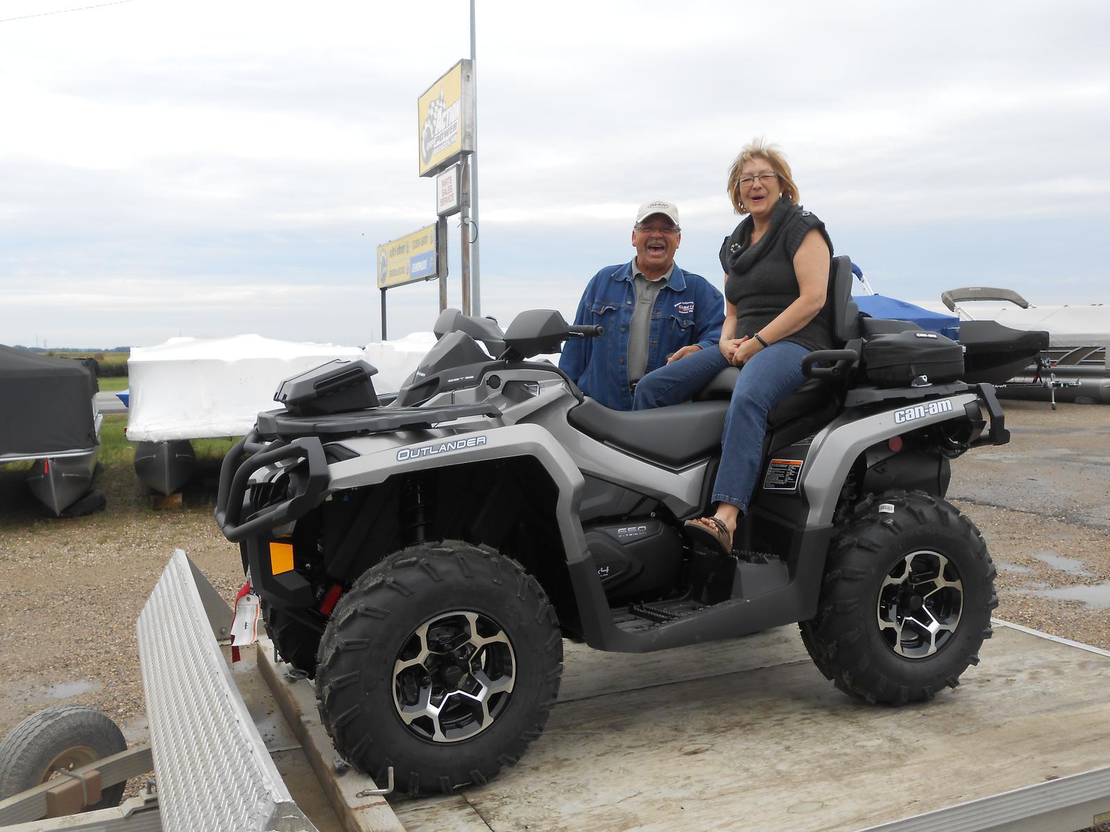 Woman seated in a gray Can-Am Outlander ATV, with a man standing beside her. 