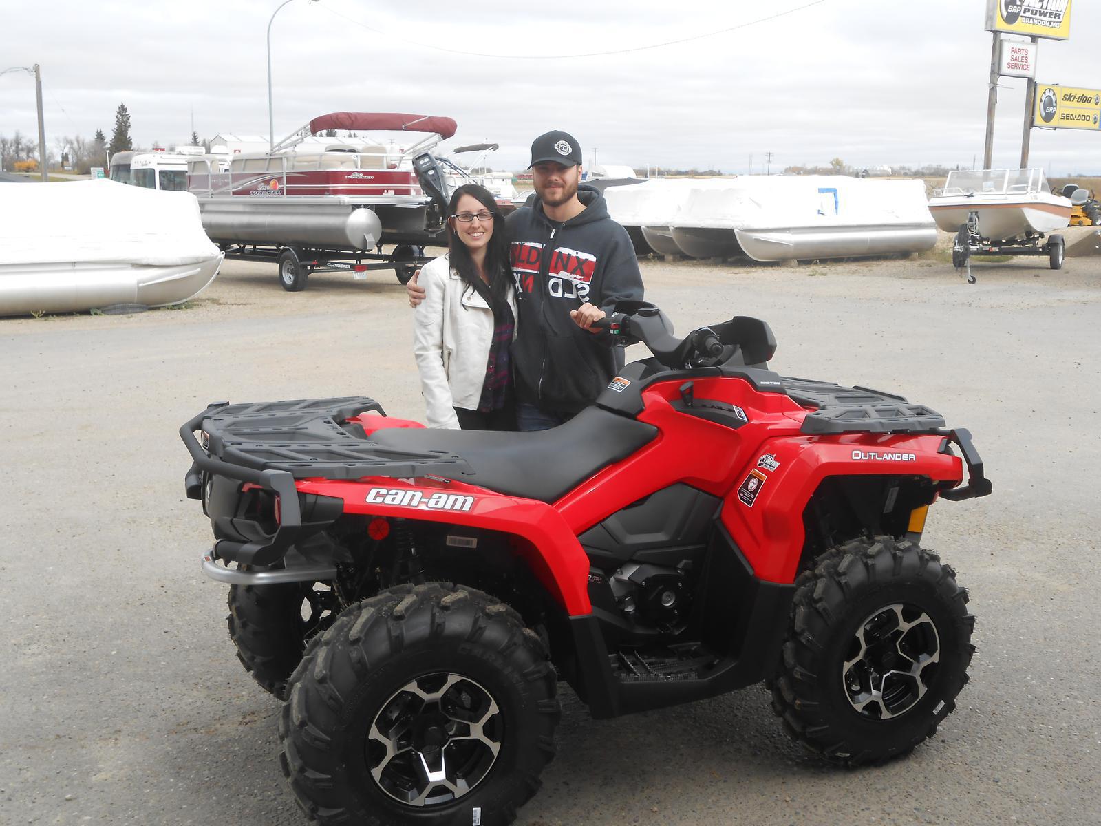 A man and a woman standing behind a red Can-Am Outlander ATV