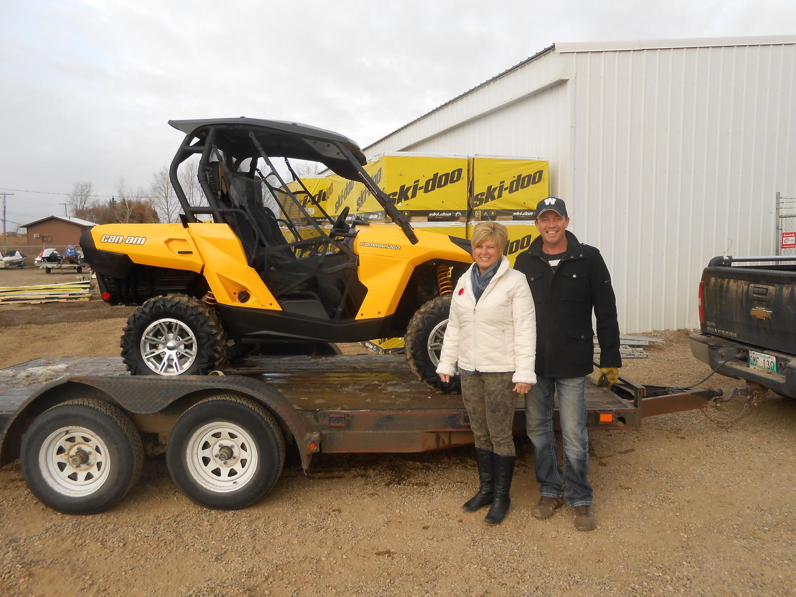 A man and a woman posing in front of a yellow Can-Am Commander UTV.