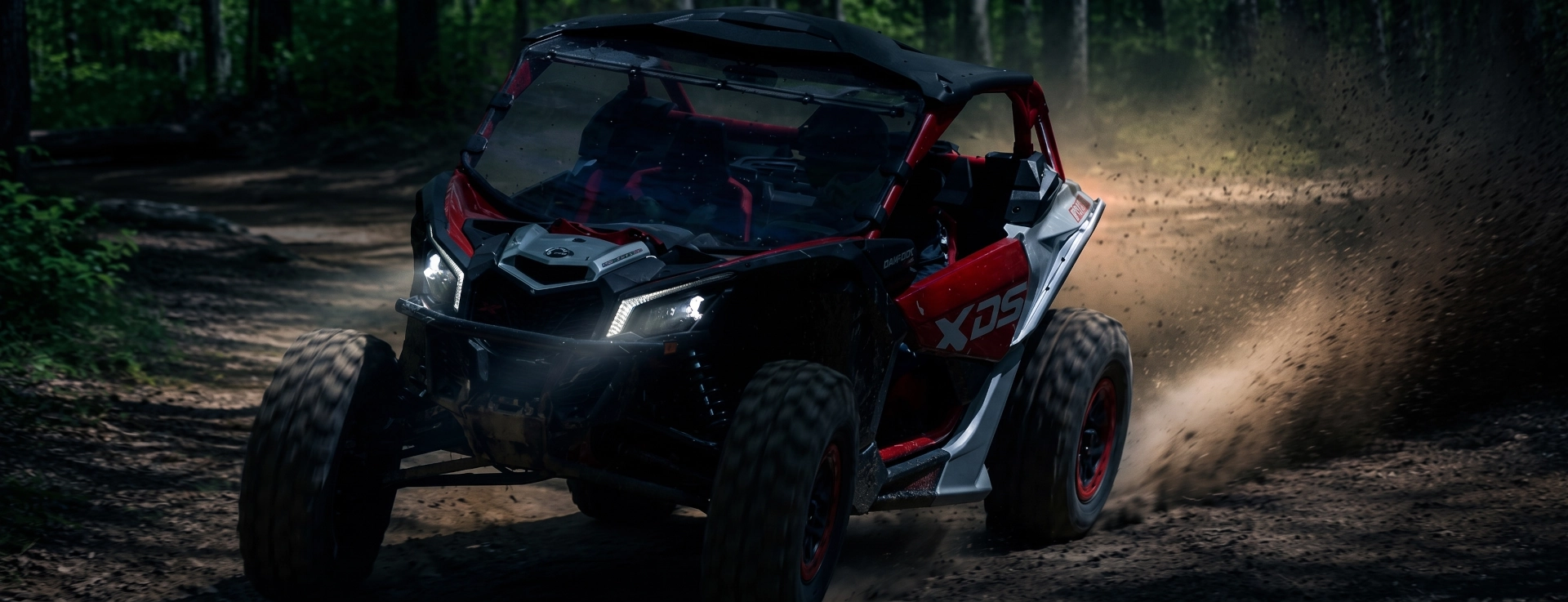 Black off-road vehicle driving along a cliff at night with powerful headlights on, followed closely by another car